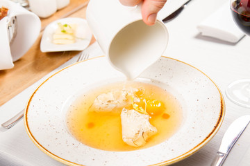 Broth with dumplings and an egg yolk being poured from a jug