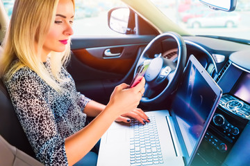 Woman using a laptop and smartphone in her car