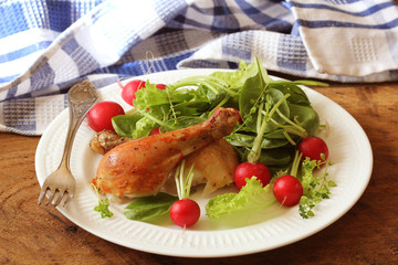 Grilled chicken legs with fresh vegetables on wooden table served on white plate . Dinner background