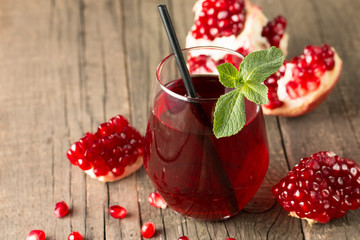 A glass of pomegranate juice with fresh pomegranate fruits on wooden table. Vitamins and minerals. Healthy drink concept.