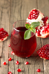 A glass of pomegranate juice with fresh pomegranate fruits on wooden table. Vitamins and minerals. Healthy drink concept.