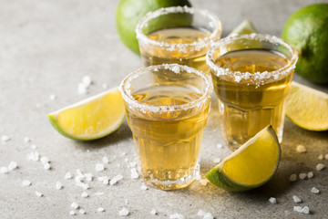 Macro focus photo of shots of golden Mexican tequila with lime and salt on wooden background. Alcoholic drink concept.