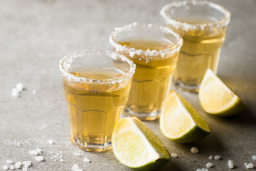 Macro focus photo of shots of golden Mexican tequila with lime and salt on wooden background....