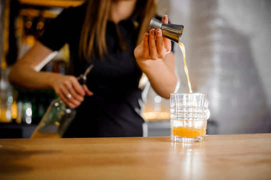 barista prepares a cocktail and pours orange juice into glass