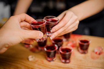 barmaid clinks glasses with a red-colored alcohol with a guest