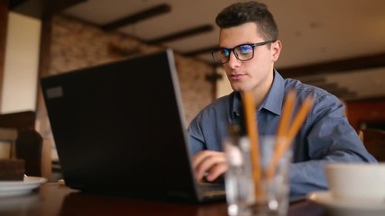 Handsome freelancer businessman in glasses diligently working on laptop in cafe. Man typing on keyboard and searches new job on internet at coffeeshop. Business concept - Powered by Adobe
