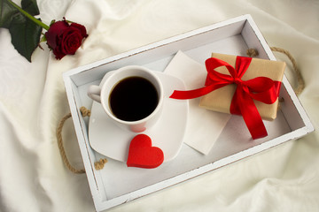Coffee and gift box  on the white wooden tray in the bed.View from above.