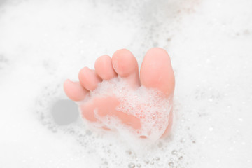 Fototapeta premium Funny barefoot. Beautiful groomed woman's foot toes in the bath bubbles. Cares about clean and soft legs skin. Lying and enjoying rest in the bathroom. Relax time. Washing concept.