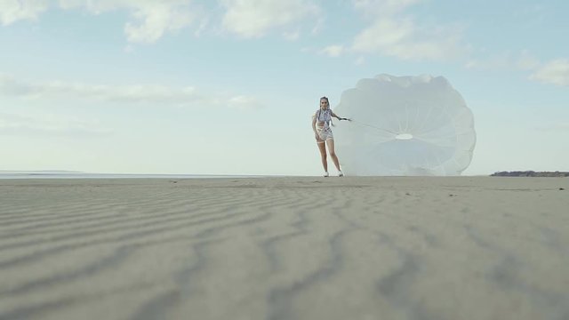 Powerful woman is trying to run out from problems on a beach with parachute. She is dragging a load of grievances,she is exhausted but moving forward