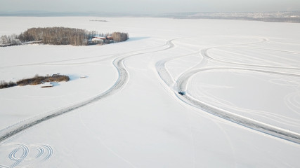 One car driving through the winter forest on country road. Top view from drone. Aerial view of snow covered road in winter, car passing by. Top view of the car traveling on snowy road