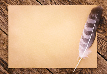 Paper with feather on the background of an old wooden table