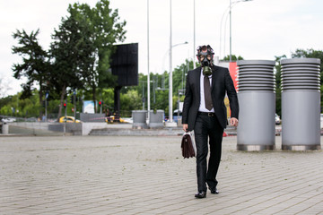 Businessman walking outdoor with briefcase wearing a gas mask on the face.
