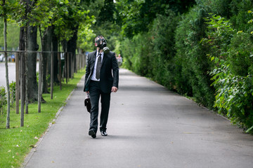 Businessman walking outdoor with briefcase wearing a gas mask on the face.