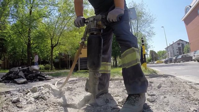Roadworks construction workers using a jackhammer to break pavement and concrete, slow motion
