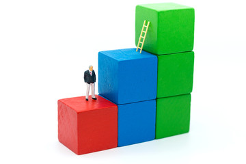 Obraz premium Miniature people: Businessmen use stairs to climb colorful wooden buildings. Image use for get better position of work.