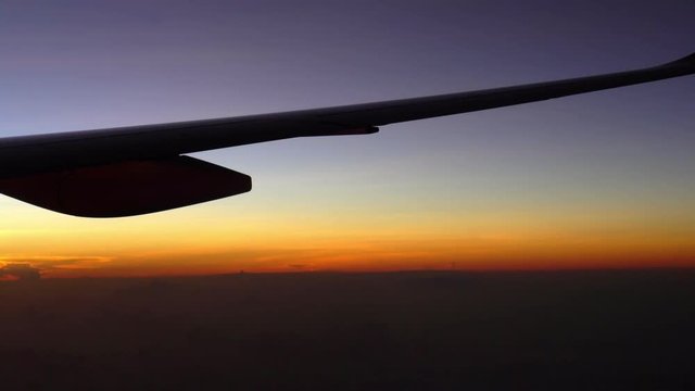 The decline or dawn is visible from a plane window. Beautifully dark blue sky. Orange dawn or decline. View of airplane wing through plane window during flight over clouds.