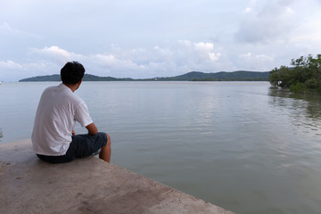 Lonely asian man sitting alone on a pier on sea in phuket thailand.