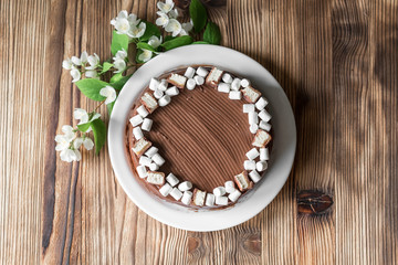 Chocolate cake, decorated with marshmallow, nougat, jasmine flowers on brown wooden table