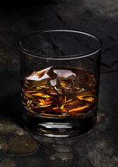 Elegant glass of whiskey with ice cubes on stone