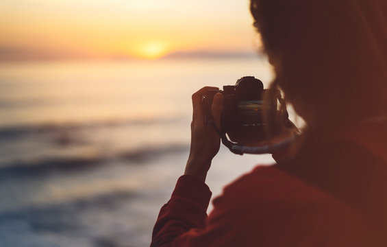Hipster hiker tourist with backpack taking photo of seascape sunset on camera on background sea, photographer enjoying ocean horizon, panoramic sunrise, traveler relax holiday concept, trip vacation