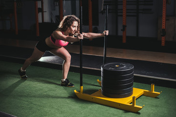 Muscular and strong young female pushing sled on grass turf. Fit woman exercising at cross fit gym.