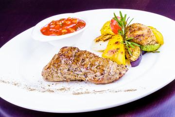 Grilled meat garnished with vegetables on white plate
