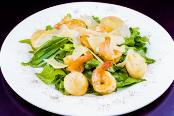 Salad with shrimps, scallops, cheese and spinach on white plate