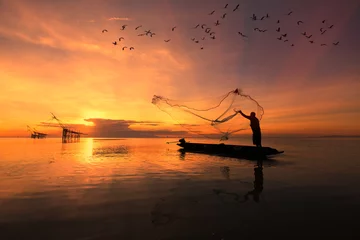 Poster de jardin Mer / coucher de soleil Pêcheur asiatique sur un bateau en bois jetant un filet pour attraper des poissons d& 39 eau douce dans la rivière naturelle tôt le matin avant le lever du soleil