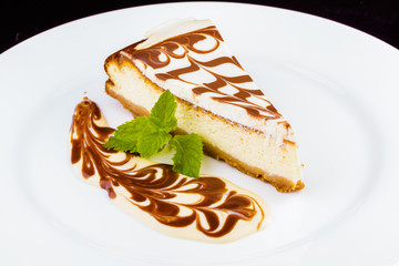 Cheesecake with chocolate topping decorated with mint on white plate