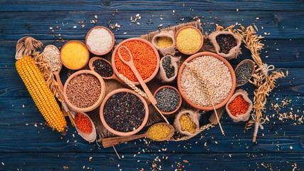 Set of Groats and Grains. Buckwheat, lentils, rice, millet, barley, corn, black rice. On a blue wooden  background. Top view. Copy space.
