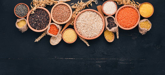 Fototapeta na wymiar Set of Groats and Grains. Buckwheat, lentils, rice, millet, barley, corn, black rice. On a black background. Top view. Copy space.