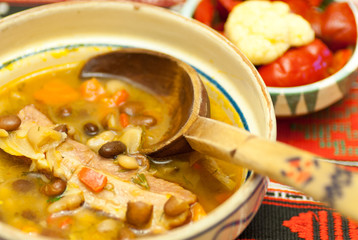 bowl with delicious bean soup with smoked meat and assorted pickles aside