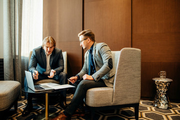 Two male employees consulting with laptop in cafe or office