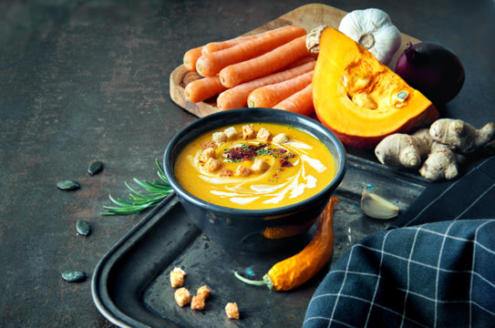 Spicy pumpkin and carrot soup with ginger, garlic, red onion and chili on dark background