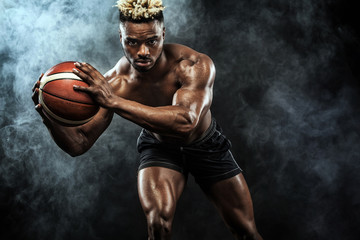 Portrait of afro-american sportsman, basketball player with a ball over black background. Fit young man in sportswear holding ball.