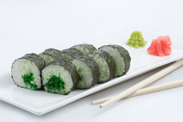 sushi or rolls in assortment on a long plate, wooden sticks, red ginger and wasabi
