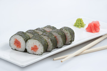 sushi or rolls with salmon on a long plate, wooden sticks, red ginger and wasabi