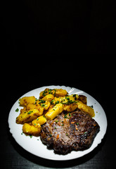 grilled meat fillet steak with fried potato in a plate on dark wooden background with copy space.