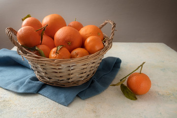 basket with fresh orange fruits and clementines with leaves on a blue napkin, gray rustic background with copy space