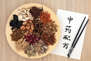Chinese traditional herbs used in alternative herbal medicine on a wooden plate and bamboo background with calligraphy script. Translation reads as chinese alternative medicine. Top view.