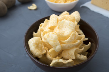 Potato chips with cheese in a plate that is located on a gray background.