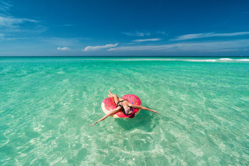 Happy beautiful brunette woman in pink hat swims on big inflatable tube at the coast of Caribbean Sea