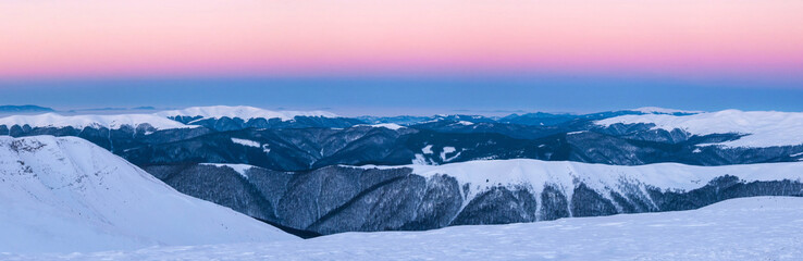 Wonderful pink sunrise in the Carpathians in winter. Panoramic photo of snow-covered summits of winter mountains in the rays of sunrise. Snow-capped mountain top like ice cream.