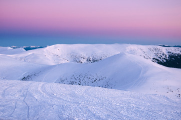 Naklejka na ściany i meble Wonderful sunrise in the Carpathians in winter. Snow-covered summits of winter mountains in the red rays of sunrise. Fresh footprints in the snow on top of the mountain.