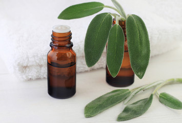 Dark glass aromatic essential oil bottle with fresh green natural sage plant leaves, white towel. 