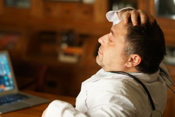 Tired overworked doctor sitting at desk and covering his eyes