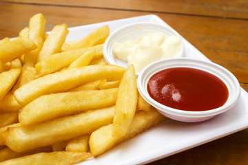 Fresh french fries served with ketchup and mayonnaise on white plate. On wooden table. Favorite junk food. Hi calories snack.