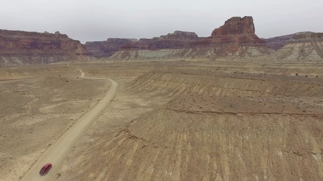 Aerial view of dirt road as truck appears driving through the desert in San Rafael Swell in Utah.