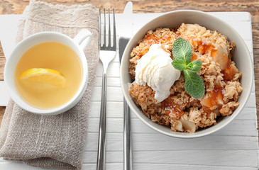 Bowl with apple crisp and ice cream on wooden board, top view