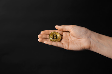 Female hand with golden bitcoin on dark background